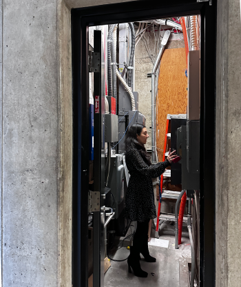 A woman inside an electrical utility closet inspecting the breakers