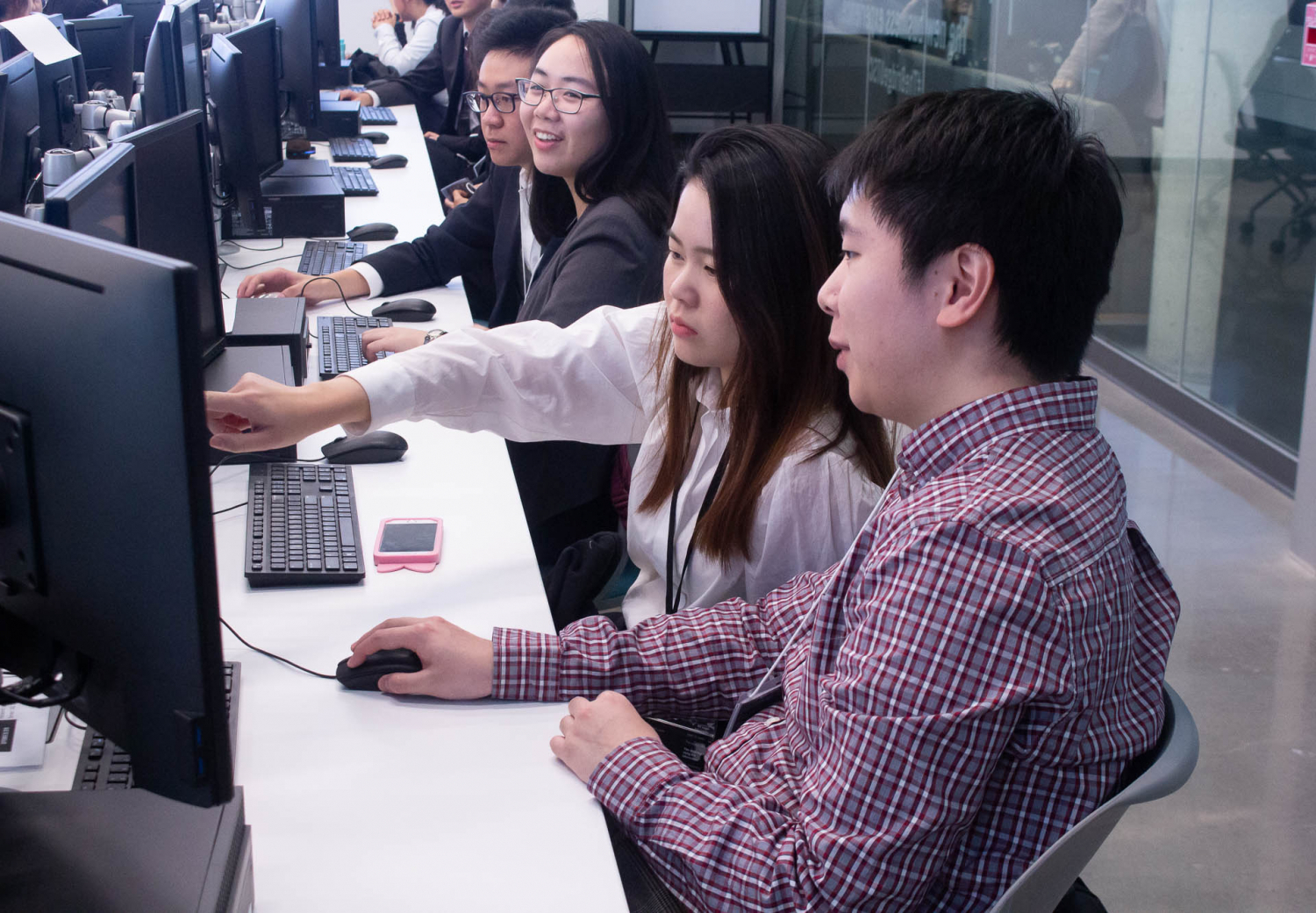 students in computer lab, talking and pointing at computer screen