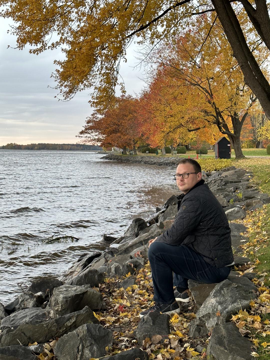 Professor Chad Cowie crouched on rocky lake shore in autumn