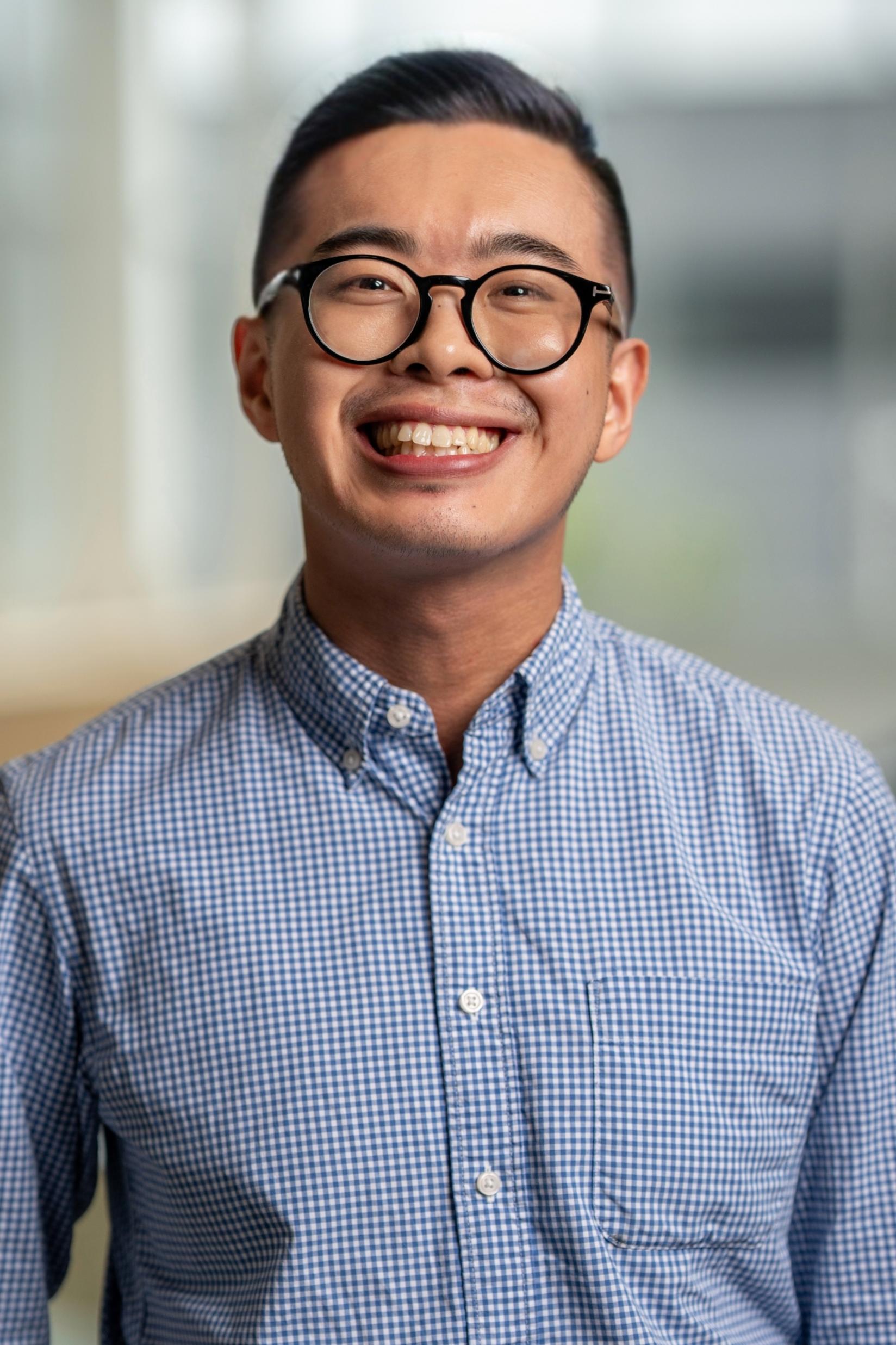 Andrew Situ smiling with glasses and checked shirt and open foyer in blurred background
