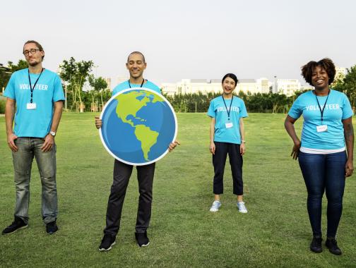 4 diverse people standing in a field with one holding a globe